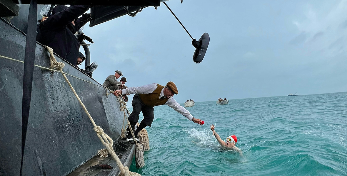 While filming a scene from Young Woman and the Sea, Trudy Ederle, played by Daisy Ridley, swims close to the ship where Jabez Wolffe, played by Christopher Eccleston, hangs over the side and hands her an apple. The crew is on the boat capturing the moment.