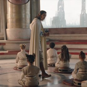 In an image from Star Wars: The Acolyte, Jedi Master Sol stands in the center of a training room in the Jedi Temple in Coruscant, speaking to the seated younglings surrounding him.