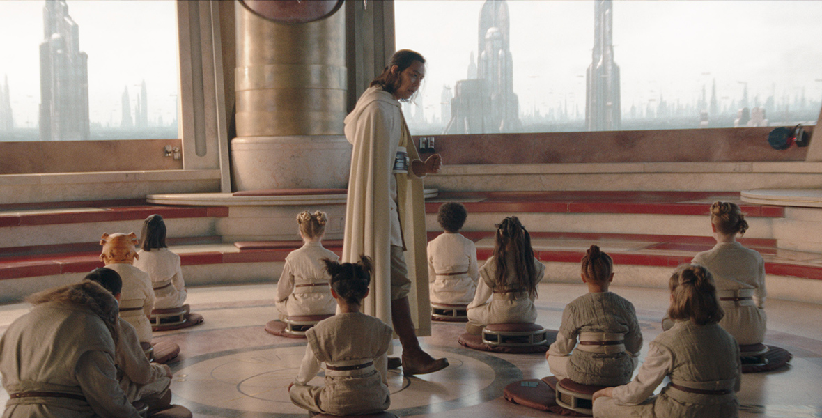 In an image from Star Wars: The Acolyte, Jedi Master Sol stands in the center of a training room in the Jedi Temple in Coruscant, speaking to the seated younglings surrounding him.