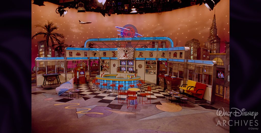 An empty stage set at Disney-MGM Studios for The All New Mickey Mouse Club, with a plane in the backdrop. Red chairs, tables, and a circular bar are visible on the set. © Disney