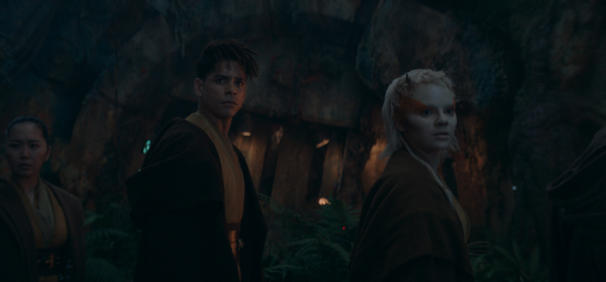 In an image from Star Wars: The Acolyte, Yord Fandar, a humanoid Jedi Master, stands next to Jecki Lon, a half-human, half-theelin Jedi padawan. Both are looking towards the camera in surprise at something offscreen.