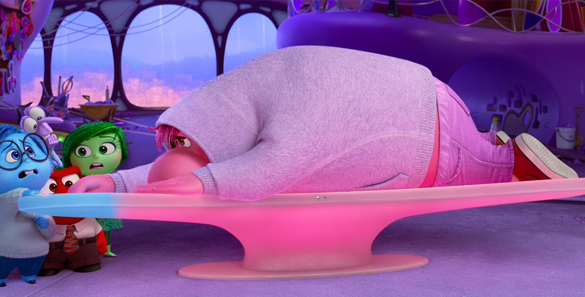 In a scene from Inside Out 2, Sadness (voiced by Phyllis Smith), Fear (voiced by Tony Hale), Anger (voiced by Lewis Black), and Disgust (voiced by Liza Lapira) stand on the left side of the Headquarters’ console. The left corner has turned blue with Sadness’s touch. Lying on his stomach on the console and turning it pink is Embarrassment (voiced by Paul Walter), clad in a gray hoodie, jeans, and red shoes. On the right side of the console stands Anxiety (voiced by Maya Hawke), looking nervously at Embarrassment. The background of the images features windows and shelves with colorful, illuminated marble balls.