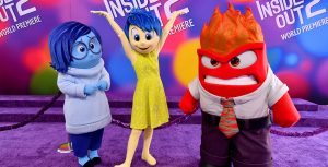 Inside Out 2 characters, left to right, Sadness, Joy, and Anger stand together in poses appropriate to their personalities at the film’s world premiere at the El Capitan Theatre in Hollywood, California, on June 10. The backdrop behind them features the film’s logo repeated in white on a multicolored background.