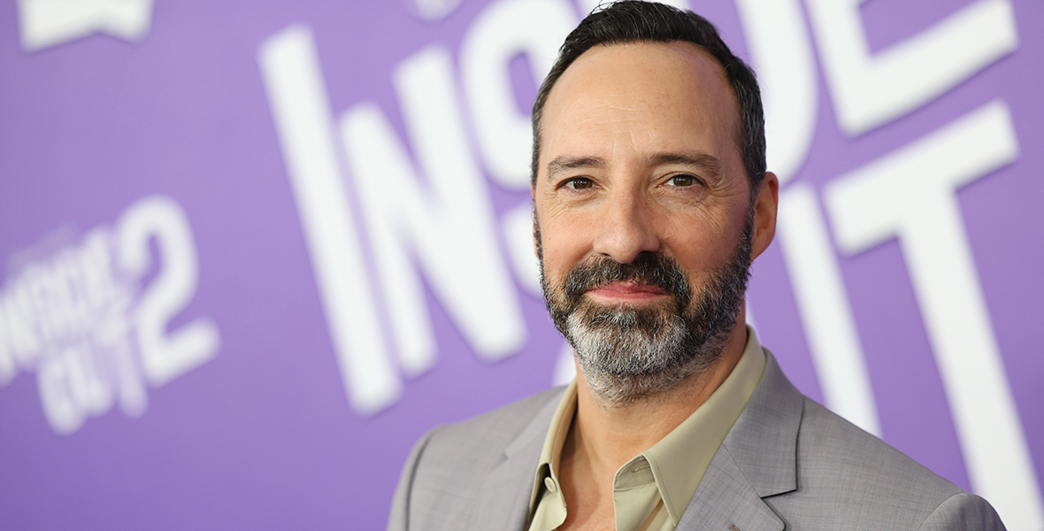 Inside Out 2 cast member Tony Hale stands in front of a backdrop with the film’s logo on it in white on purple at the film’s world premiere at the El Capitan Theatre in Hollywood, California, on June 10. He’s wearing a gray sport jacket over a green shirt.