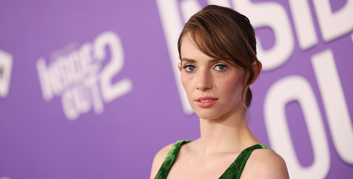 Inside Out 2 cast member Maya Hawke stands in front of a backdrop with the film’s logo on it in white on purple at the film’s world premiere at the El Capitan Theatre in Hollywood, California, on June 10. She’s wearing a dark green low-cut gown.