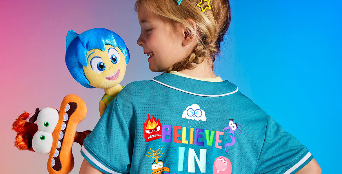 A young girl wearing a baseball jersey is seen holding the Joy and Anxiety plushes celebrating Disney and Pixar’s Inside Out 2.