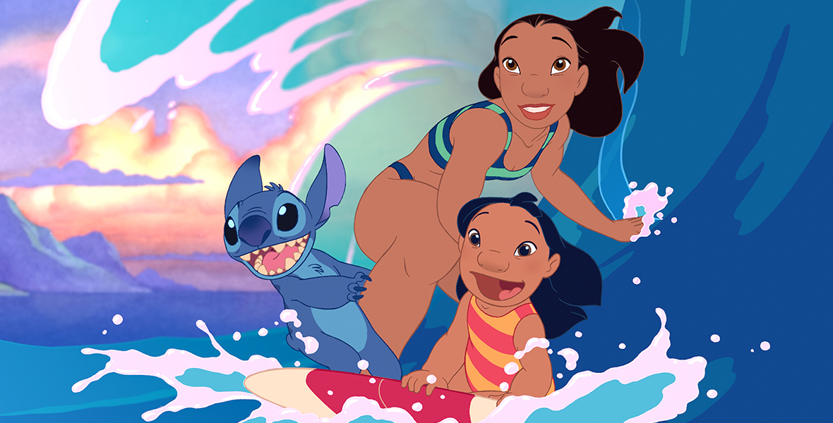 In a scene from Lilo & Stitch, Stitch (voiced by Chris Sanders), an extraterrestrial life-form resembling a blue koala, Lilo (voiced by Daveigh Chase), and Nani (voiced by Tia Carrere) are surfing. A wave hovers above them in various hues of blue, and the background features mountains and clouds. Lilo is wearing a red and orange striped one-piece swimsuit, while Nani is wearing a teal and dark blue bikini.