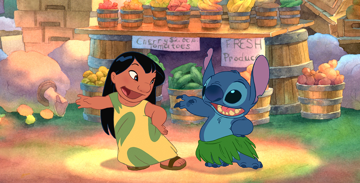 In a scene from Lilo & Stitch, Stitch (voiced by Chris Sanders), an extraterrestrial life-form resembling a blue koala, and Lilo (voiced by Daveigh Chase) are dancing in an outdoor market. Stitch is wearing a green Hawaiian leaf hula skirt, while Lilo is wearing a yellow tunic with green leaf patterns and brown sandals. In the background, there are barrels of fresh produce, such as cherry tomatoes. Two signs read “Cherry tomatoes two dollars a pound.” and “Fresh Produce.” 