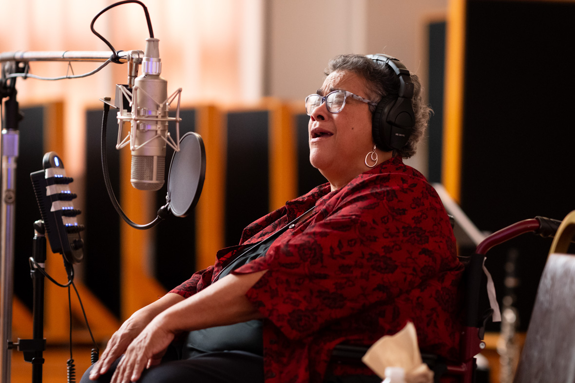 Leah Chase sits in a music studio, singing into a microphone with her eyes closed.