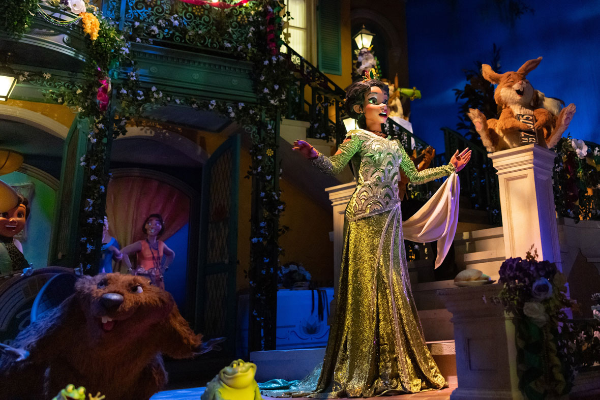 In the finale of Tiana’s Bayou Adventure, Princess Tiana sings in front of a colorful building, surrounded by critters performing music. To her right, a rabbit sits on a stair railing, playing a license plate like a washboard.