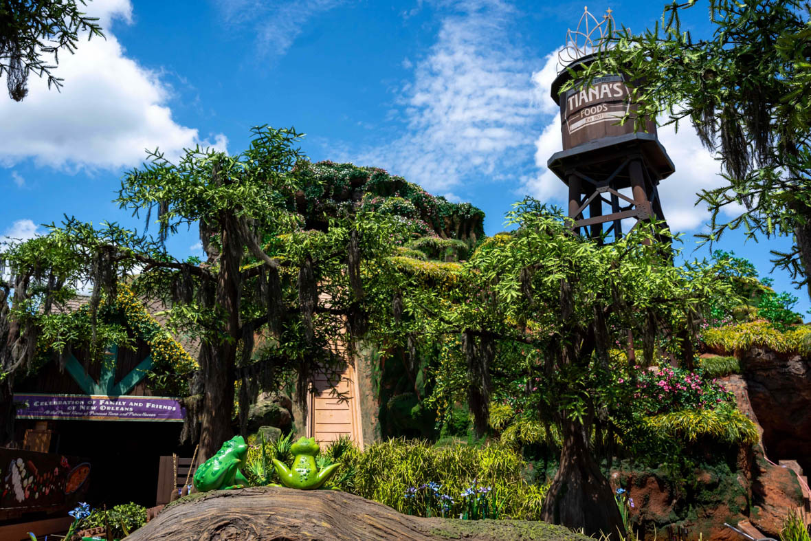 The exterior of Tiana’s Bayou Adventure, facing the attraction’s 50-foot drop. In the bottom of the image, two frogs sit on a log with their backs to the camera.