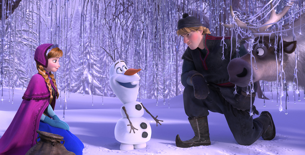 In an image from Frozen, a snowman, Olaf, stands in the middle of a wintery wonderland and smiles as Anna (left) and Kristoff (right) kneel beside him. A reindeer, Sven, stands to Kristoff’s left.