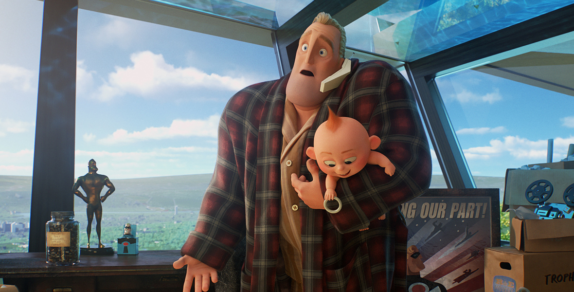 In an image from Incredibles 2, a frustrated Bob aka Mr. Incredible wears a plaid robe and pajamas. He is talking on the phone while holding baby Jack-Jack. They are surrounded by boxes of memorabilia.