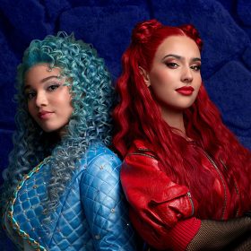 Chloe, played by Malia Baker, stands back-to-back with Red, played by Kylie Cantrall, in a promotional photo for Descendants: The Rise of Red. Chloe has curly blue hair and wears an all blue fencing outfit. Red has red hair and wears a red leather costume.