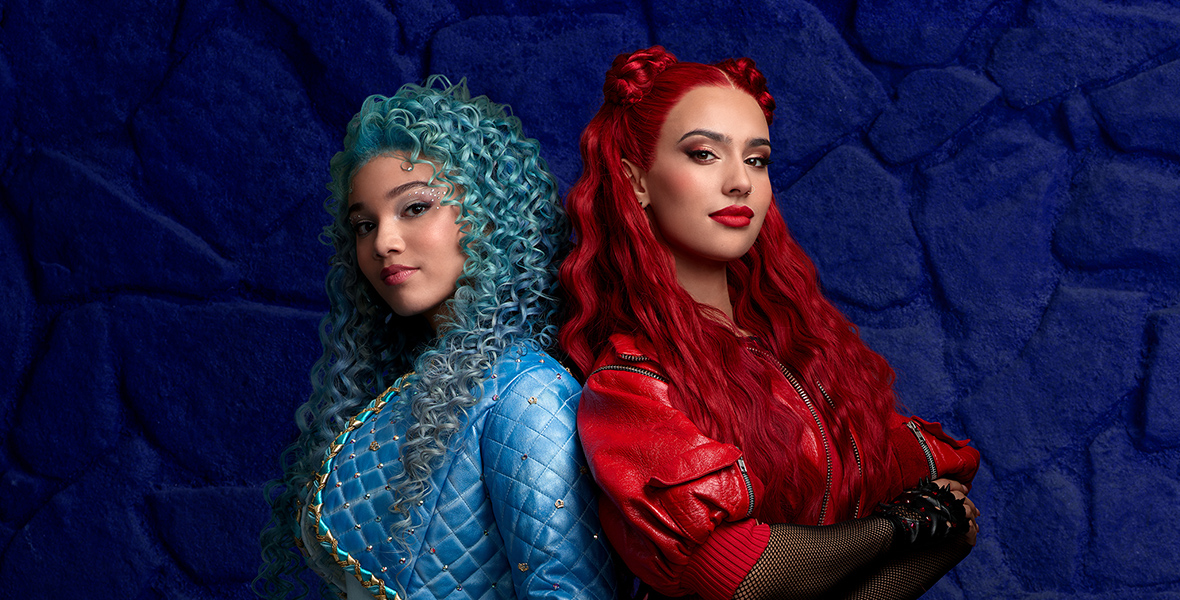 Chloe, played by Malia Baker, stands back-to-back with Red, played by Kylie Cantrall, in a promotional photo for Descendants: The Rise of Red. Chloe has curly blue hair and wears an all blue fencing outfit. Red has red hair and wears a red leather costume.