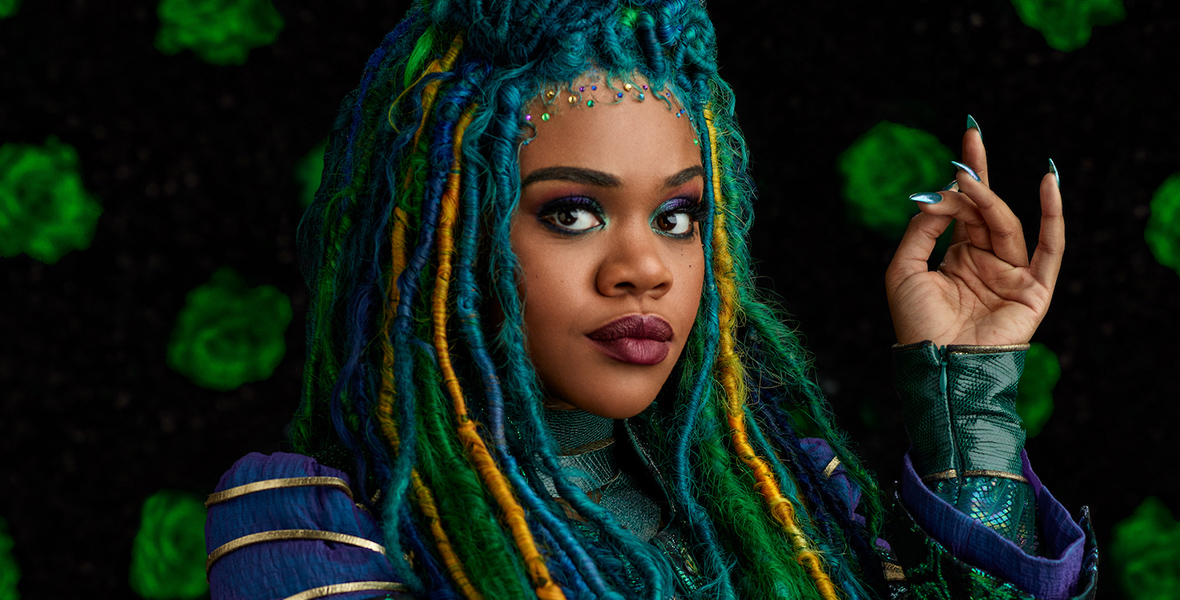 In a promotional image for Disney Channel’s Descendants: The Rise of Red, Uliana, played by Dara Reneé, has blue, green, and gold dreadlocks. She is wearing an ornate robe made of mixed materials in various shades of purple, blue, green, and gold.