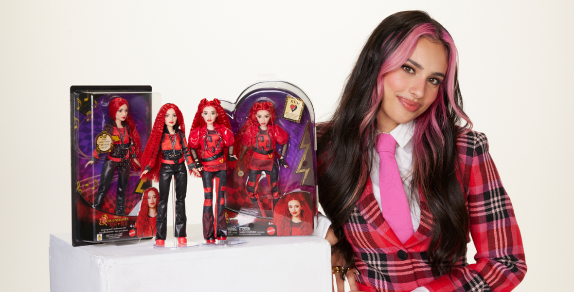 Kylie Cantrall, who plays Red in Descendants: The Rise of Red, poses with four Red fashion dolls. She is wearing a red plaid jacket.