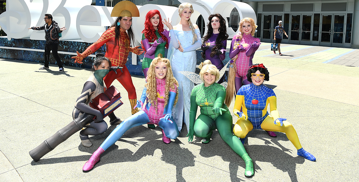 An image showing fans from the previous D23 Cosplay Meet-Ups. Eight cosplayers dress up as variations of Spider Man across Disney universes, while one cosplayer in the center is dressed as Elsa, with blonde hair and an icy blue gown to match.