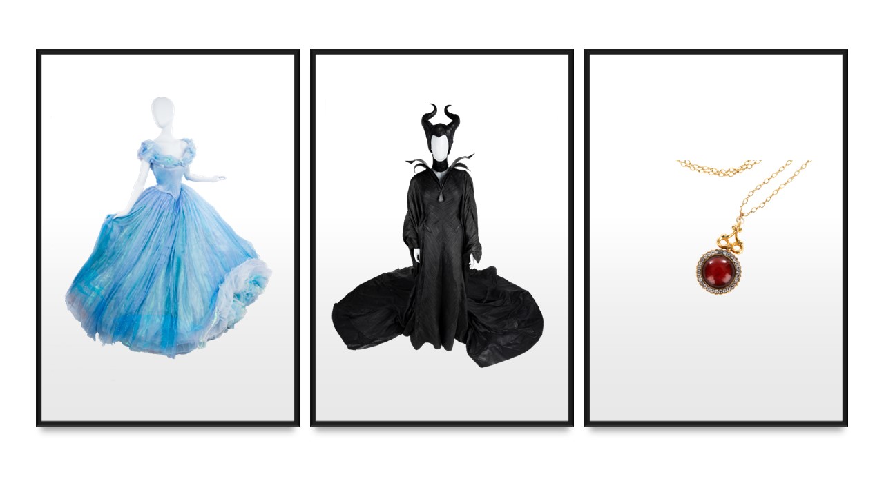 From left to right - A faceless mannequin wears Cinderella’s magnificent blue ballgown from the 2015 live-action film. A faceless mannequin wears Maleficent’s terrifying ensemble consisting of a black gown, cape, choker, and headpiece. Cruella’s necklace from the 2021 live-action film, made of a gold chain and large red circular pendant surrounded by smaller silver stones, dangles. All three are pictured against a plain white backdrop.