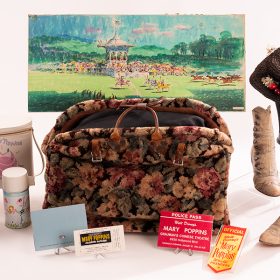 A collection of Mary Poppins paraphernalia arranged around Mary’s carpet bag, at the center, includes Poppins dolls and pins, a ticket from the premiere, a hat and two pairs of shoes worn by star Julie Andrews, and more.