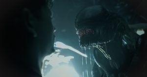 A Xenomorph bares its silver teeth at a frightened man.