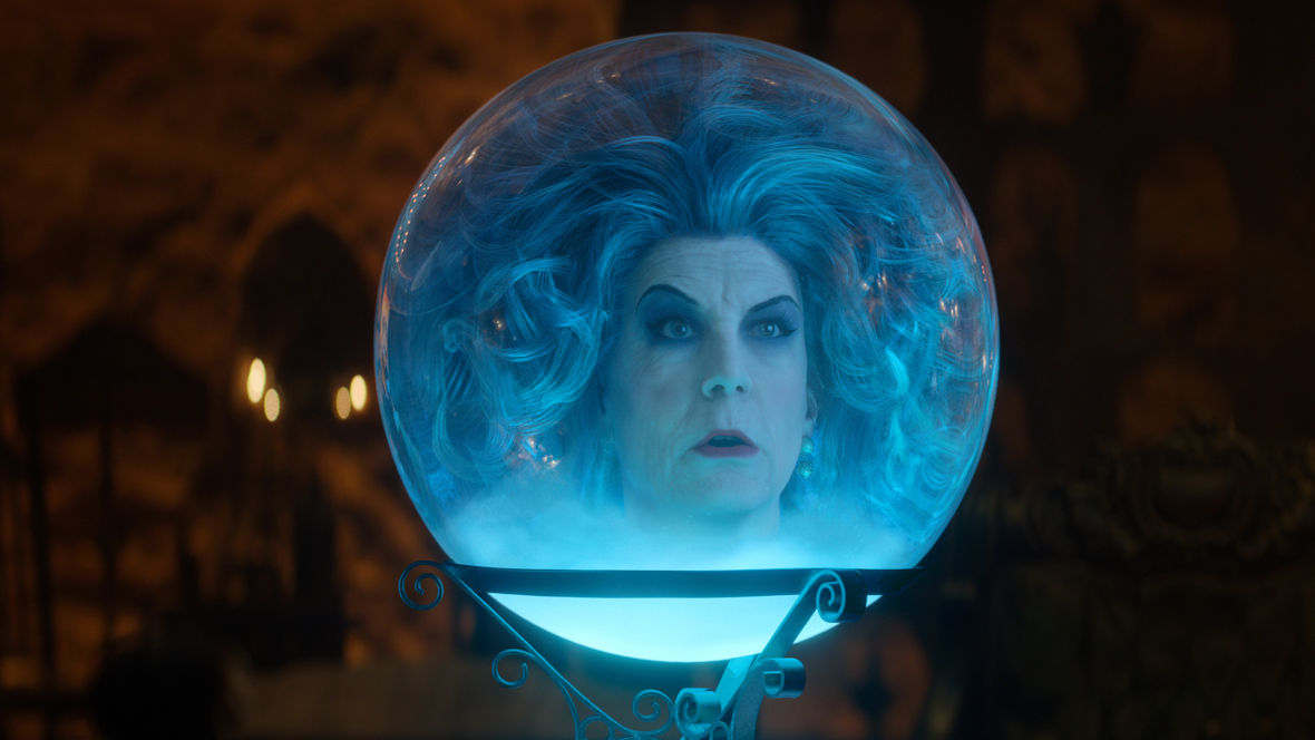 In a scene from Haunted Mansion (2023), Madame Leota (Disney Legend Jamie Lee Curtis) appears trapped in a crystal ball with hues. She has voluminous blue hair, blue eyeshadow with a black liner, and dark red lipstick. 