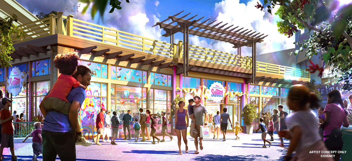 A vibrant, colorful storefront of the Wonderful World of Sweets shop at Downtown Disney District. The entrance features a white sign with pink and blue letters, and various sweets including cupcakes and cookies decorating the store’s windows. Families walk toward the entrance, and the background features trees and a clear sky.