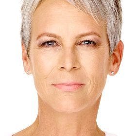 Disney Legend Jamie Lee Curtis sports short silver hair, wearing subtle makeup and small stud earrings, looking directly at the camera with a neutral expression against a plain white background.