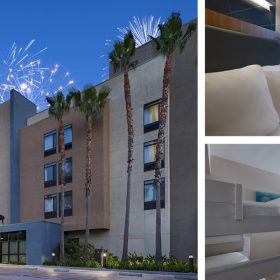 Exterior view of the SpringHill Suites by Marriott with fireworks lighting up the sky in the background. The hotel has a modern design with tall palm trees in front. On the right, two smaller images show the interior of the hotel rooms. One room features a comfortable bed with a window view of the fireworks, while the other room has bunk beds and a desk area, with another bed visible in the background.