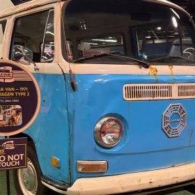 A Dharma bus in worn condition, featuring rust stains and the distinctive Dharma Initiative logo on the front on the show floor.