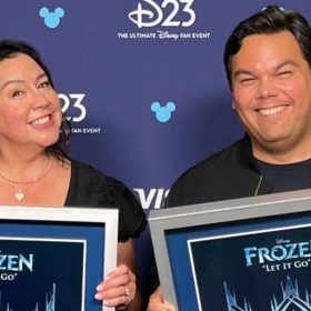 Kristen Anderson-Lopez and Robert Lopez each hold an RIAA Diamond plaque backstage at D23: The Ultimate Disney Fan Event.