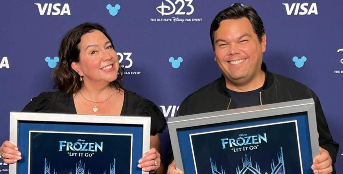 Kristen Anderson-Lopez and Robert Lopez each hold an RIAA Diamond plaque backstage at D23: The Ultimate Disney Fan Event.