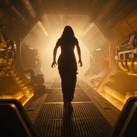 Kay (Isabela Merced) walks through a corridor on a spaceship. Her silhouette is illuminated by a bright orange light.