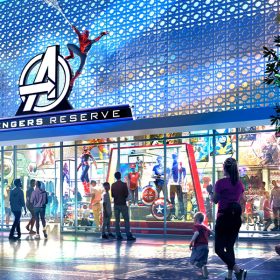 A vibrant, modern storefront of the Avengers Reserve shop at Downtown Disney District, featuring a large Avengers logo above the entrance. Spider-Man swings above the logo, and a life-sized Hulk statue bursts through a wall on the left side, with visitors admiring the scene. The interior of the store is brightly lit, showcasing various Marvel merchandise, including costumes and memorabilia.