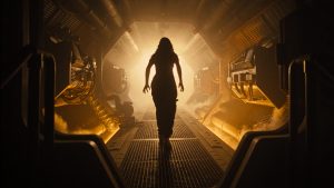 Kay (Isabela Merced) walks through a corridor on a spaceship. Her silhouette is illuminated by a bright orange light.