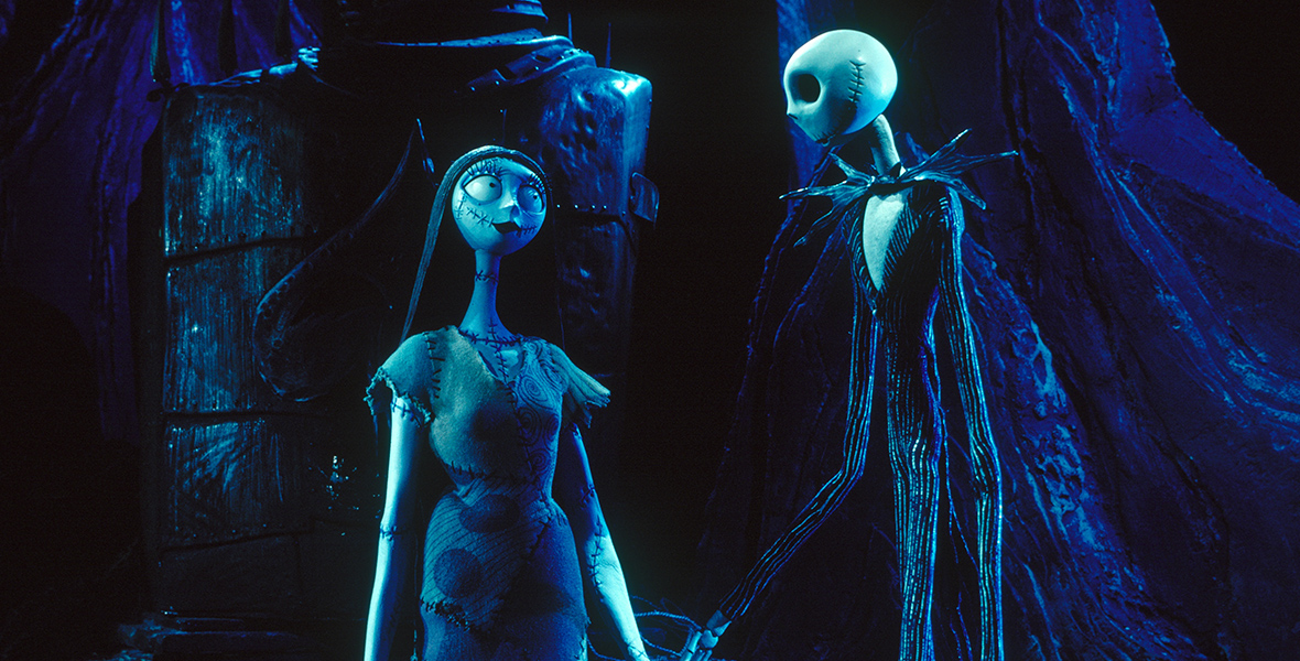 In a scene from The Nightmare Before Christmas, Sally (voiced by Catherine O'Hara), a blue-skinned rag doll, gazes at Jack Skellington (voiced by Danny Elfman and Chris Sarandon), a tall skeleton dressed in a black pin-striped suit. Sally and Jack are holding hands and looking at each other. The background features large, clay-like objects in black and dark blue hues.