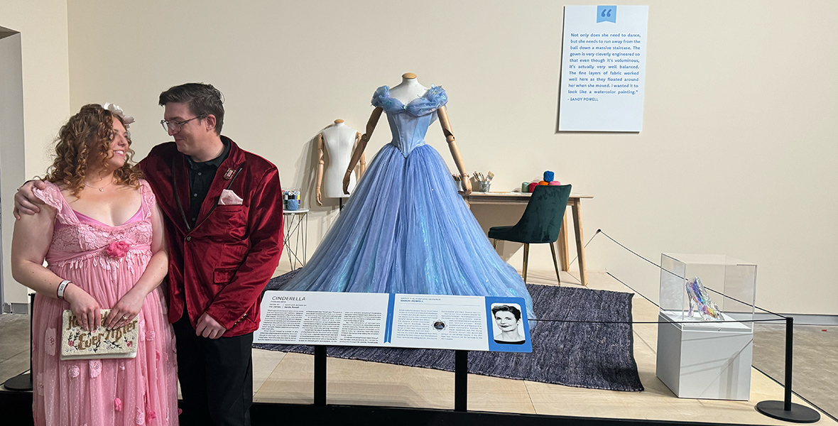 he happy newly engaged couple posing lovingly in front of the live-action Cinderella dress.