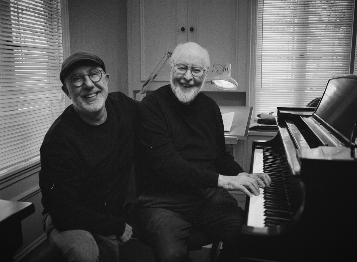 A black and white photo of Laurent Bouzereau sitting next to John Williams at the piano