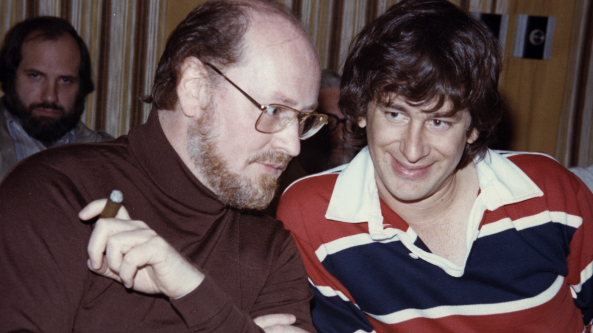 John Williams holds a cigar and sits next to Steven Spielberg in 1977.