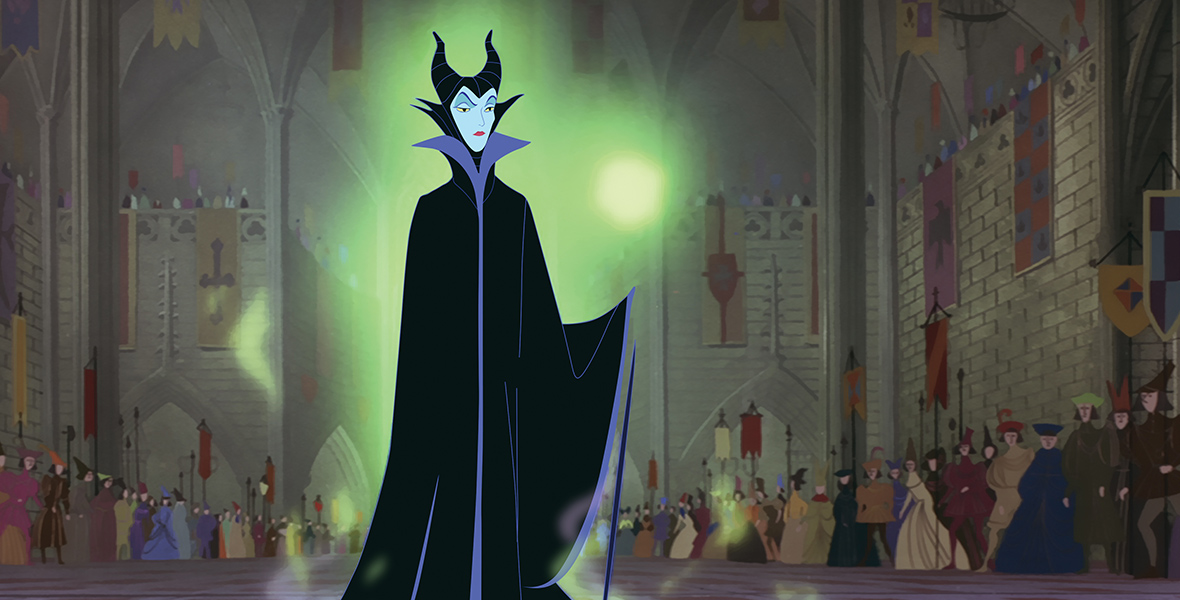 In an image from Sleeping Beauty (1959), Maleficent (voiced by Eleanor Audley) wears a black gown with a high, pointed collar accented by purple details and her signature black horns. She holds a magical scepter with a glowing green orb at the top, as green magic swirls around her. The background shows the interior of a stone castle adorned with flags, where people lean away towards the walls in fear.