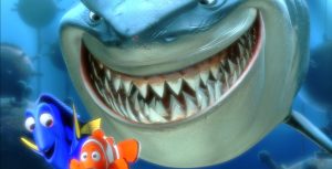 In a scene from Finding Nemo, Dory (voiced by Ellen DeGeneres), a blue tang fish, and Marlin (voiced by Albert Brooks), a clownfish, swim away from Bruce (voiced by Barry Humphries), a great white shark, who grins widely as the two fish move in front of him. The scene takes place underwater, with naval mines visible in the background. 