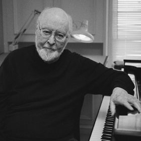 A black and white photo of John Williams sitting at the piano.