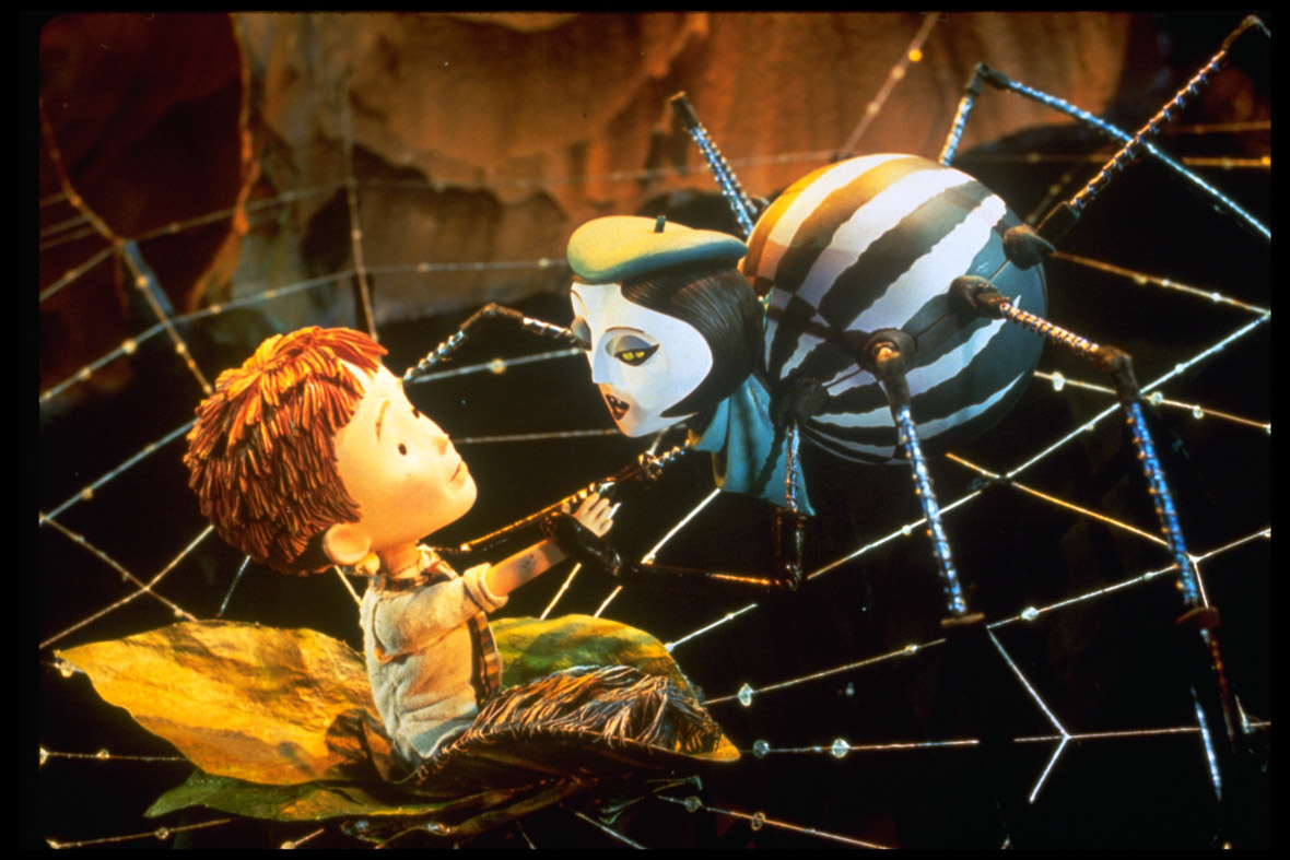 In a scene from James and the Giant Peach, James (voiced by Paul Terry)—now transformed into a doll-like boy—sits at the center of a web. Miss Spider (voiced by Susan Sarandon), an anthropomorphic wolf spider, approaches him. With short black hair, two golden eyes on either side of her head, and a striking black-and-white body, she holds James’ right arm, wrapping another of her legs around his neck.