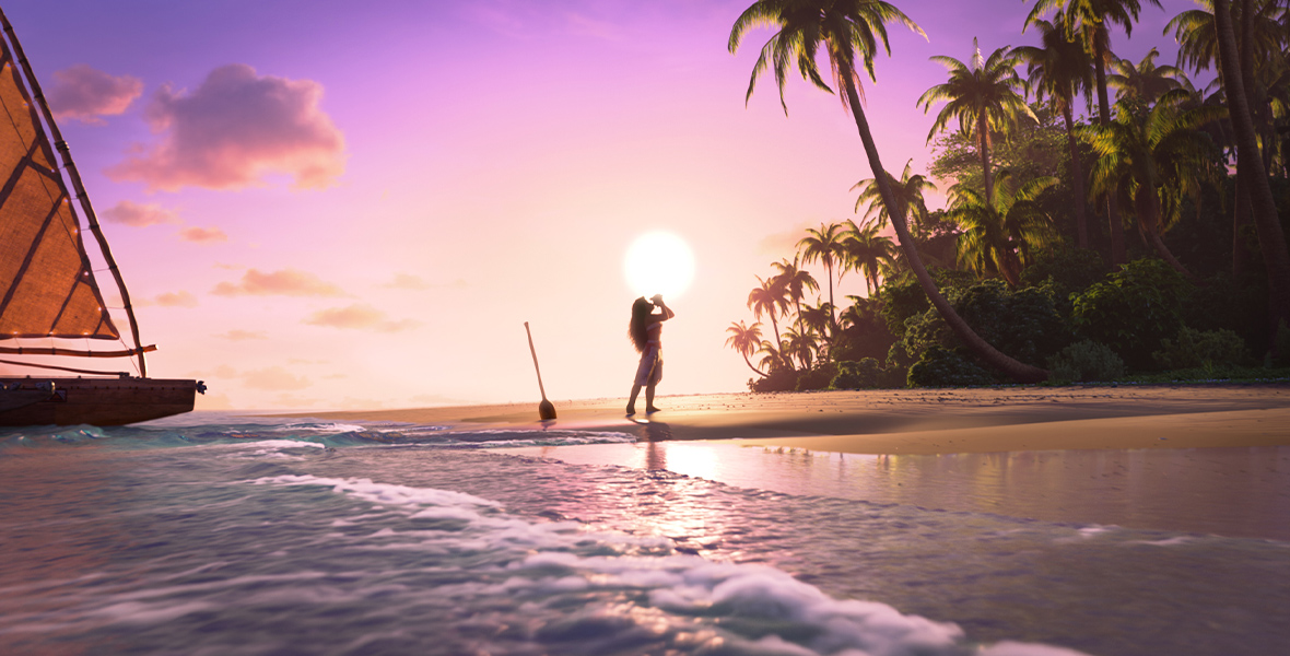 In an image from Walt Disney Animation Studios’ Moana 2, Moana (voiced by Auli‘i Cravalho) is seen in silhouette standing on the beach, blowing into a conch shell. The sun is behind her and almost setting; an oar is sticking out of the sand nearby, and her canoe can be seen near the shore on the left. Palm trees and other greenery can be seen on the right.