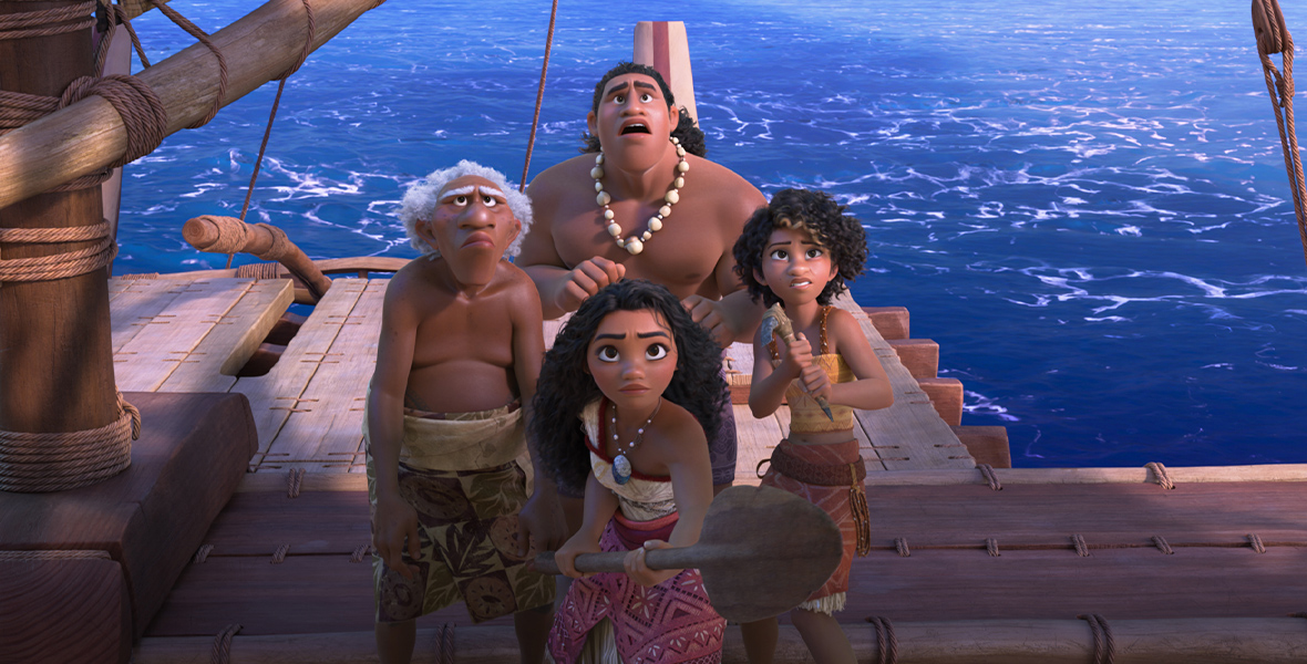 In an image from Walt Disney Animation Studios’ Moana 2, Moana (voiced by Auli‘i Cravalho) is surrounded by her crew (l-r) Kele (voiced by David Fane), Moni (voiced by Hualālai Chung), and Loto (voiced by Rose Matafeo) as they stand on their canoe; all four are looking up at something off camera, with concerned looks on their faces. Moana is holding onto an oar, and Loto is holding onto some sort of axe-type tool.