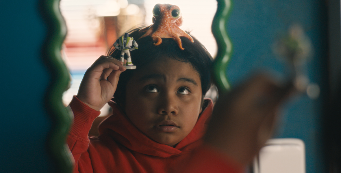 A young boy, with an orange octopus on his head, plays with a Buzz Lightyear toy.