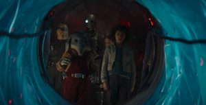 In a scene from Star Wars: Skeleton Crew, KB, played by Kyriana Kratter, Neel, played by Robert Timothy Smith, the droid SM-33, voiced by Nick Frost, Fern, played by Ryan Kiera Armstrong, and Wim played by Ravi Cabot-Conyers, huddle around an opening.