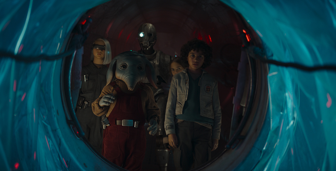 In a scene from Star Wars: Skeleton Crew, KB, played by Kyriana Kratter, Neel, played by Robert Timothy Smith, the droid SM-33, voiced by Nick Frost, Fern, played by Ryan Kiera Armstrong, and Wim played by Ravi Cabot-Conyers, huddle around an opening.