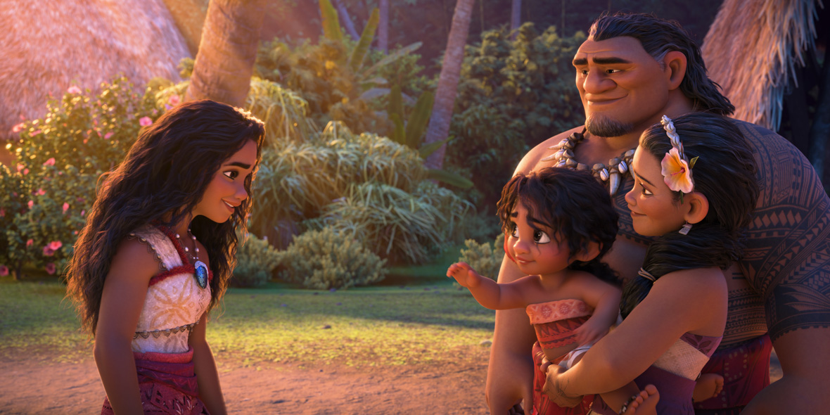 In an image from Walt Disney Animation Studios’ Moana 2, Moana (voiced by Auli‘i Cravalho), left, is standing with her family—sister Simea (voiced by Khaleesi Lambert-Tsuda), mother Sina (voiced by Nicole Scherzinger), and father Tui (voiced by Temuera Morrison), right. Sina is holding Simea in her arms, and Simea is reaching out to Moana; they are all smiling at each other. Lush island greenery is seen behind them.