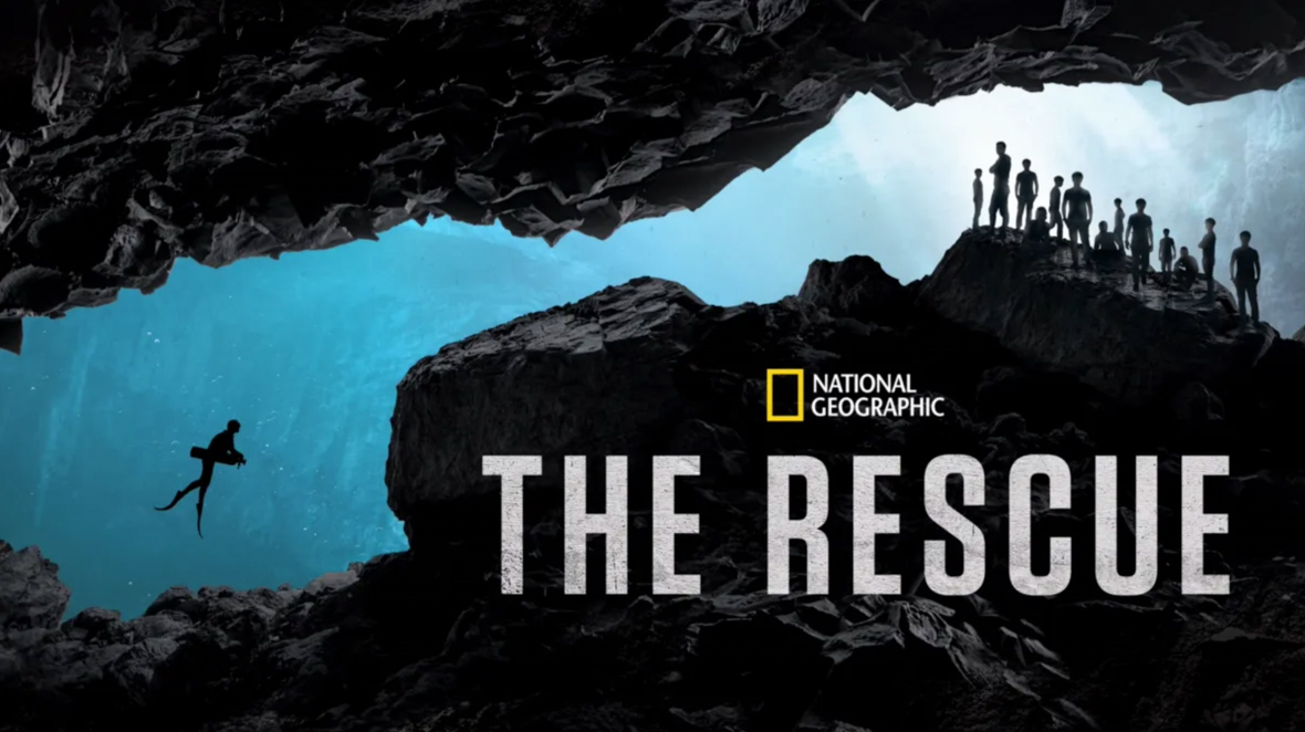 A key art image for National Geographic’s The Rescue. At left, a solo diver is making their way through a narrow cave-like space underwater. At right, a group of people is standing in another part of this “cave,” waiting for the diver to arrive. Below the group and set against a rock-style background is the National Geographic logo and the title of the film.